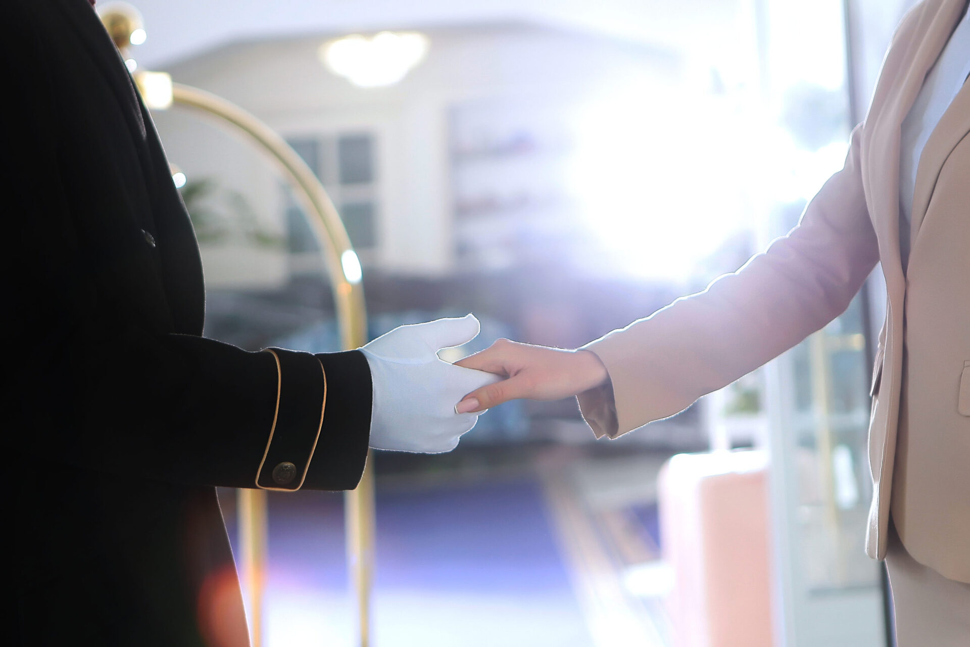 A uniformed doorman greets a guest at the hotel. A doorman in white cotton gloves.